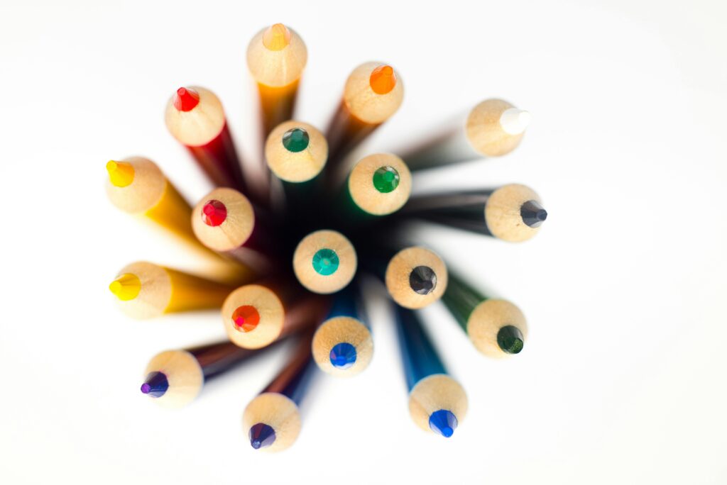 Top view of brightly colored pencils arranged in a circular pattern on a white background.